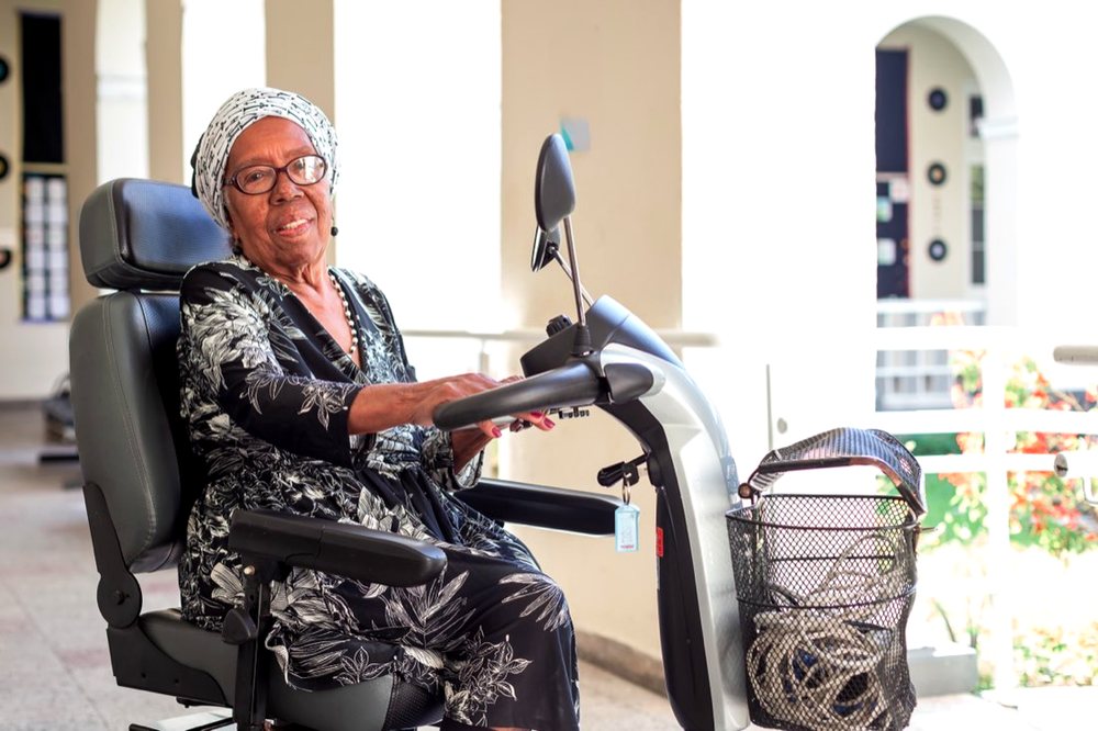 Moradora sorrindo em sua cadeira motorizada na varanda do Asilo.
