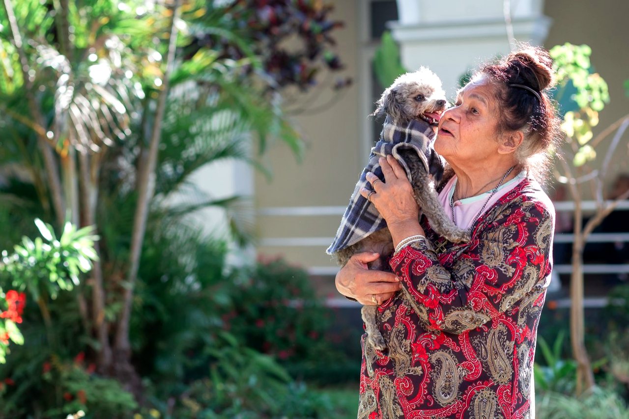 Moradora segurando no colo o seu cachorro no jardim.